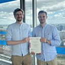 Ruben Diestelkamp und Florian Egger halten – stellvertretend für das gesamte Team des Abschnitts 5.2 (Großenbrode) – den Planfeststellungsbeschluss in den Händen.
