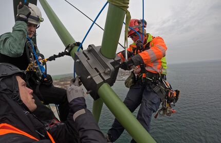 Arbeiter mit Helm und Schutzausrüstung arbeiten an einer Seilklemme an der Fehmarnsundbrücke.