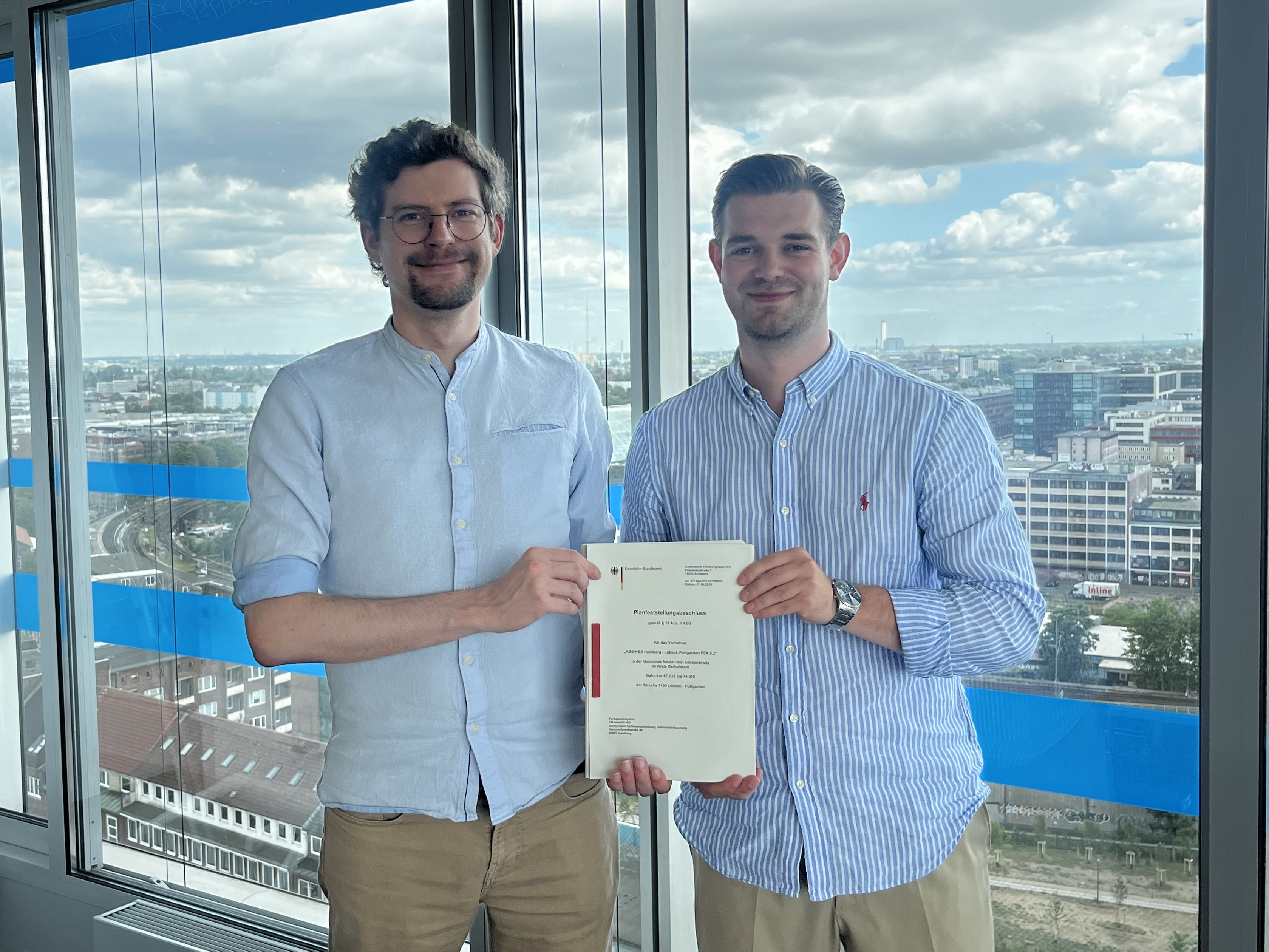 Ruben Diestelkamp und Florian Egger halten – stellvertretend für das gesamte Team des Abschnitts 5.2 (Großenbrode) – den Planfeststellungsbeschluss in den Händen.