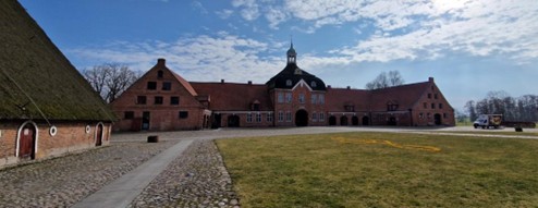 vor einer grünen Wiese steht ein roter Gutshof