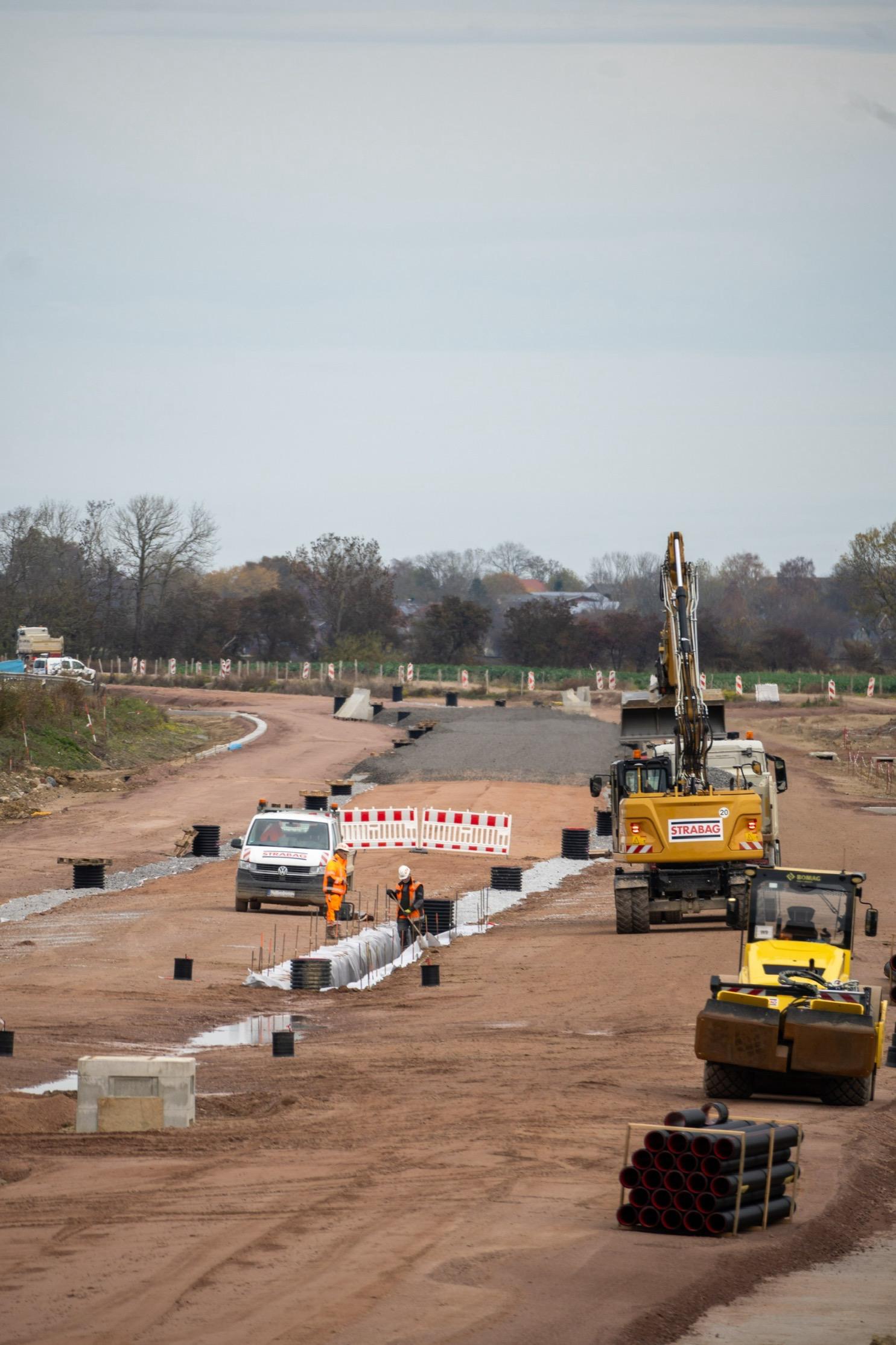 Baustellenfahrzeuge auf Erde, im Hintergrund eine Fläche mit Schotter