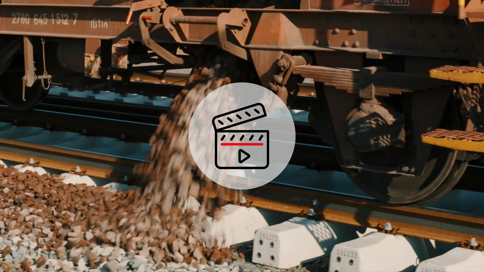Nahaufnahme: Zug lädt Schotter auf Gleisen ab. Davor ein Video-Symbol