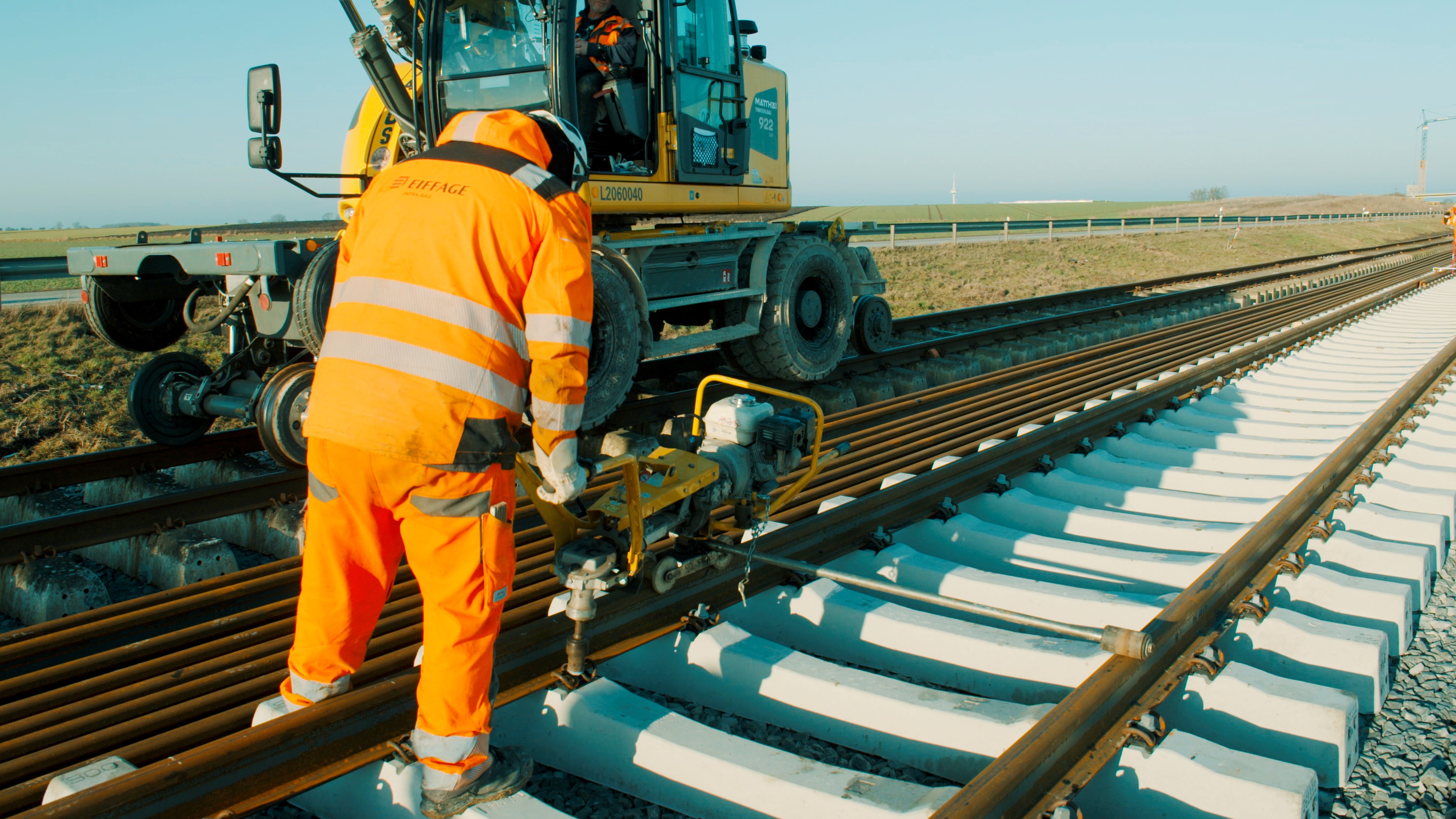 Ein Arbeiter in orangener Sicherheitskleidung schraubt Schienen auf Schwellen