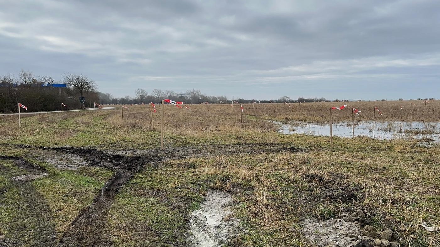 Holzpfähle mit Flatterband auf einem Acker mit Pfützen