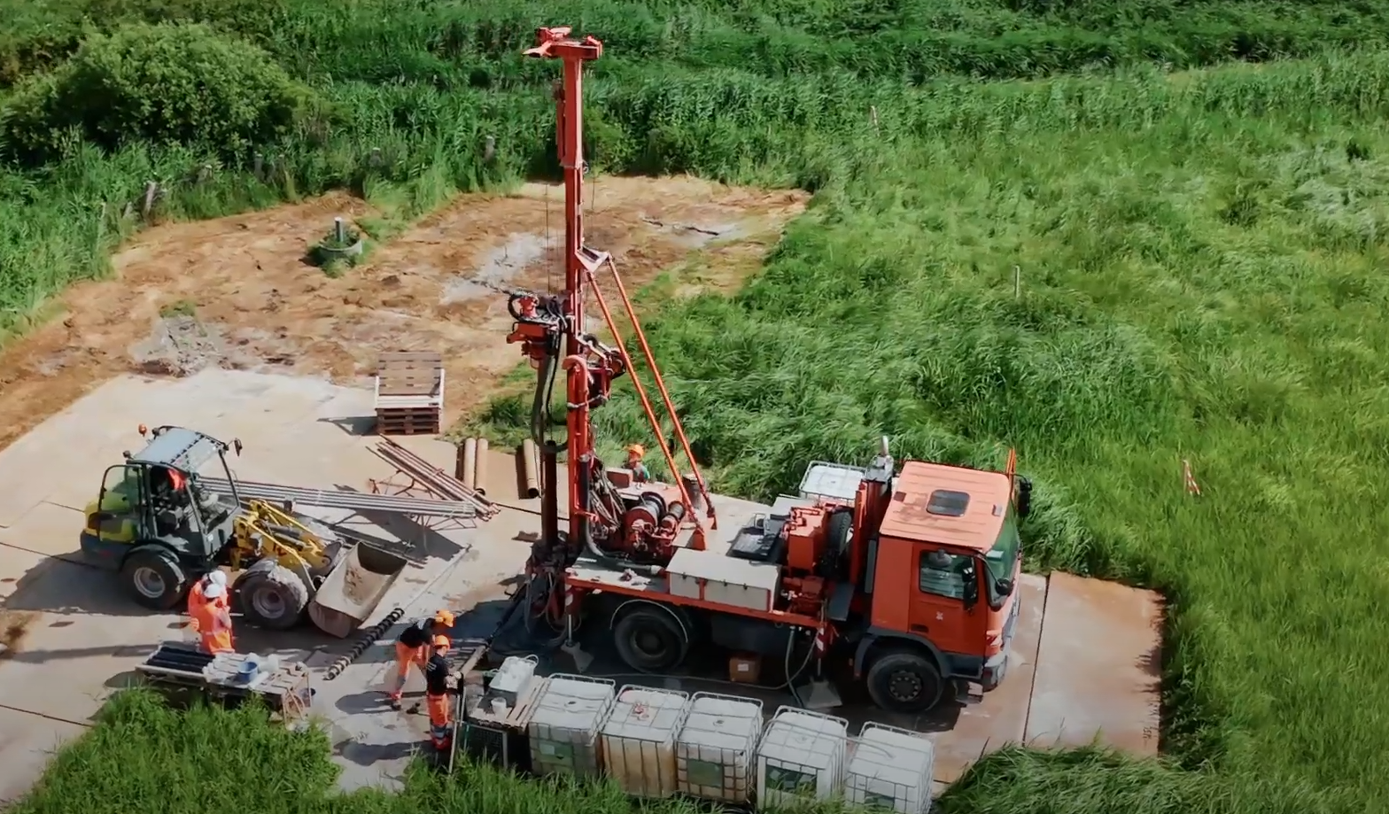 Zwei Baufahrzeuge stehen auf einem Feld und fünf Arbeiter führen Bohrungen durch