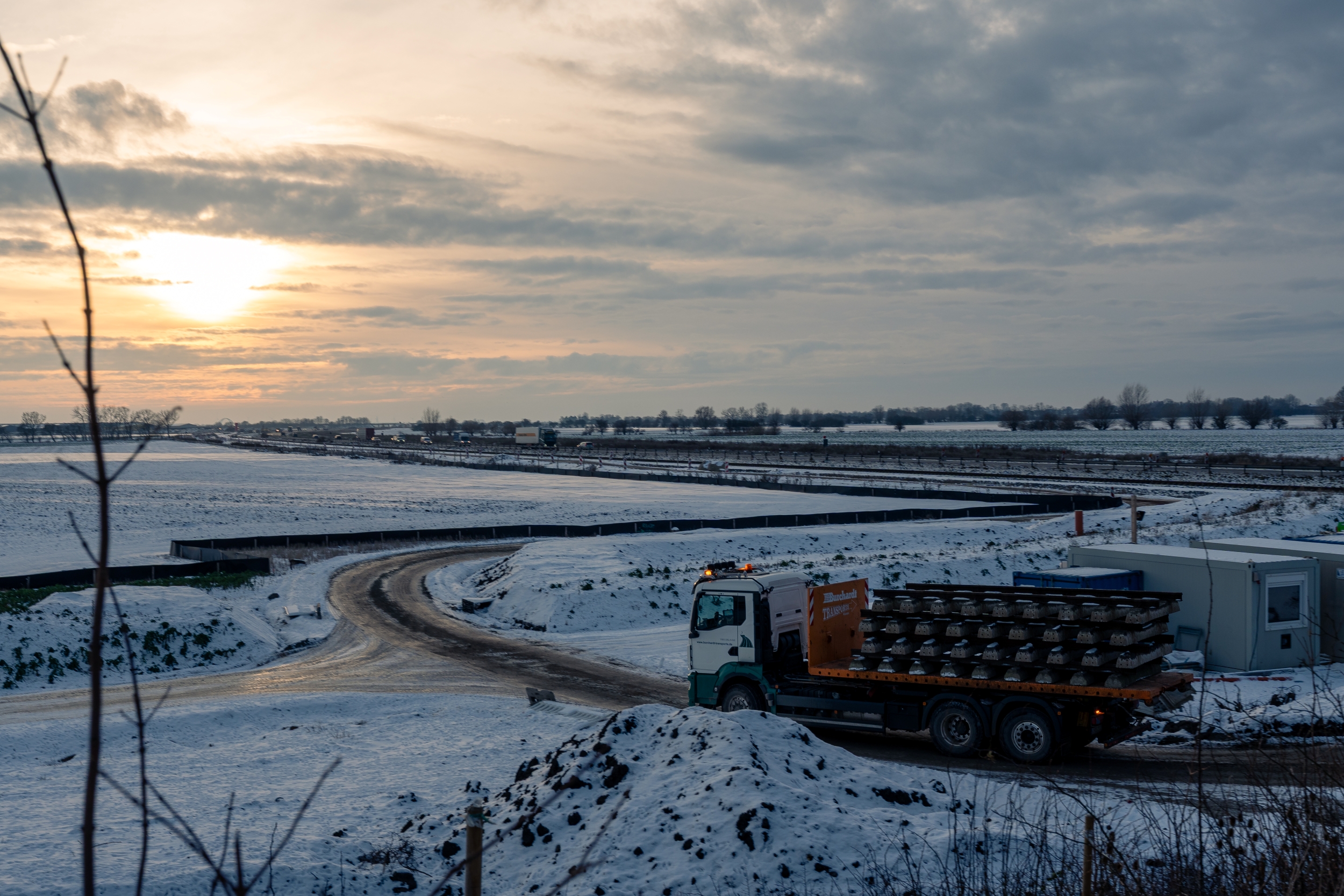 Ein LKW beladen mit Gleisen fährt bei Sonnenuntergang im Schnee