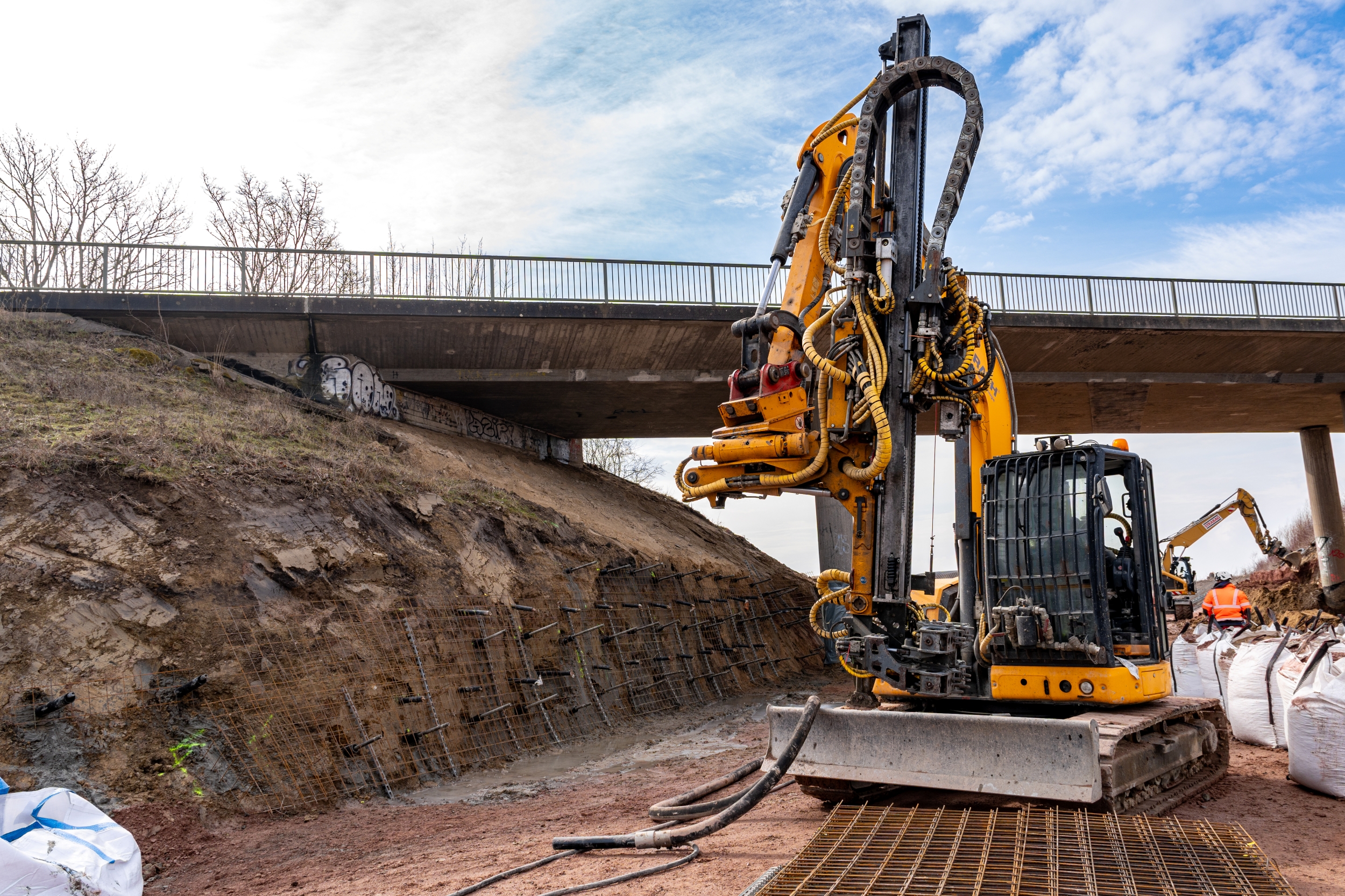 Eine Bewehrung wurde an eine Böschung angelehnt, davor ein gelbes Baufahrzeug